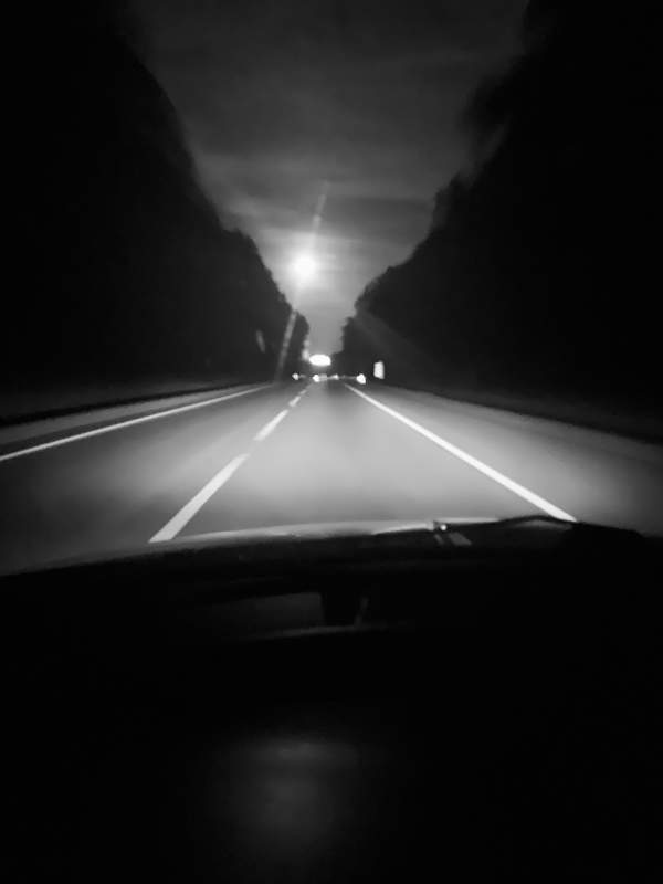 Driving along a highway at night with the moon shining overhead.